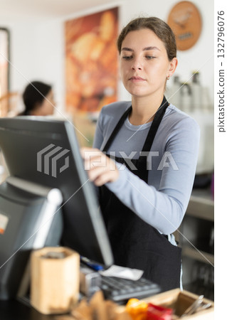 Attentive young waitress checking orders on monitor in cafeteria Attentive young waitress checking orders on monitor in cafeteria 132796076