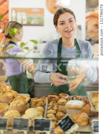 Young woman putting pastries in display case in cafe Young woman putting pastries in display case in cafe 132796078