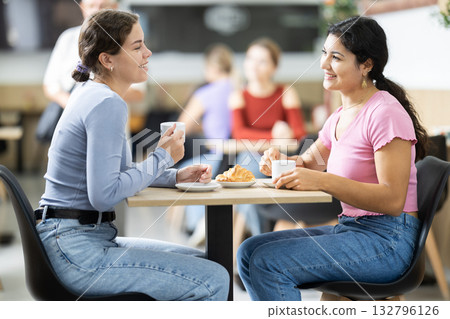 Two young girls talking over coffee and croissant in cafeteria 132796126