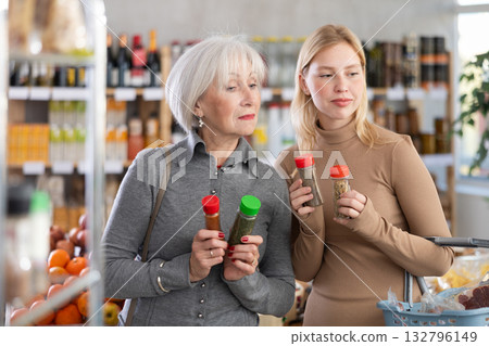 Girl and grandmother buyers examine good, doubt and choose spices and seasonings herbs in store Girl and grandmother buyers examine good, doubt and choose spices and seasonings herbs in store 132796149