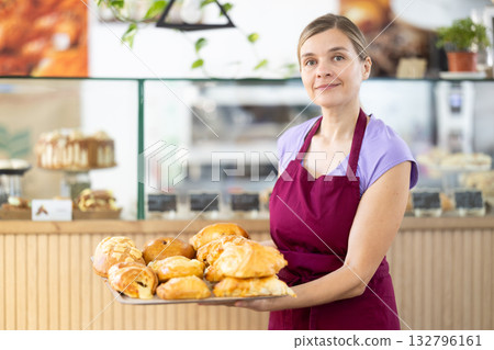 Positive female cafe employee carries tray with fresh croissants 132796161