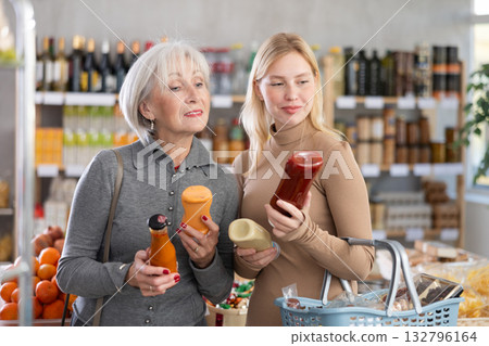 Girl and grandmother buyers examine good, doubt and choose between varieties sauce in store Girl and grandmother buyers examine good, doubt and choose between varieties sauce in store 132796164