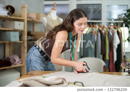 Female fashion designer cutting fabric into pattern pieces 132796209