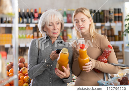 Girl and grandma scan QR code, take reading juice label using phone camera in shop 132796220