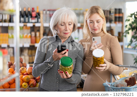 Elderly mother and her adult daughter scan QR code on jar canned green olives label together to check expiration date Elderly mother and her adult daughter scan QR code on jar canned green olives label together to check expiration date 132796221