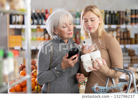 Girl and grandma scan QR code, take reading yogurt label using phone camera in shop Girl and grandma scan QR code, take reading yogurt label using phone camera in shop 132796237