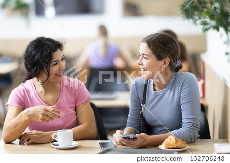 Two young girls talking over coffee and croissant in cafeteria Two young girls talking over coffee and croissant in cafeteria 132796248