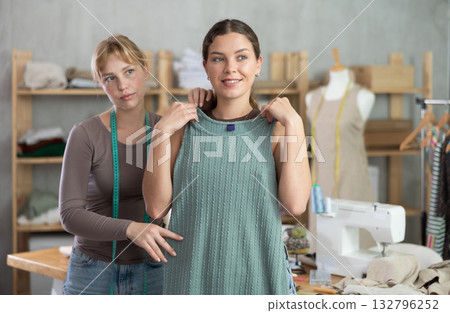 Female client and dressmaker checking tailored gown fit in studio 132796252