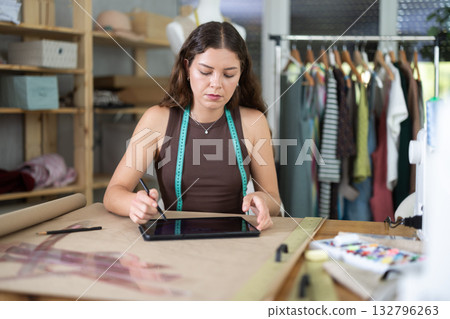 Tailor drawing fashion design on tablet in workshop 132796263