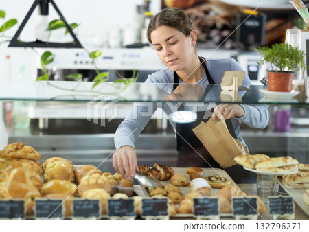 Attentive young seller putting pastries in paper bag Attentive young seller putting pastries in paper bag 132796271
