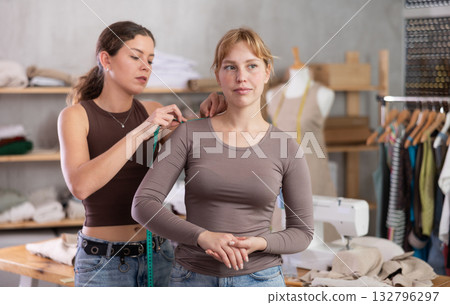 Young tailoress measuring female client in sewing workshop 132796297