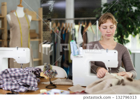 Young female dressmaker working with sewing-machine in tailor's workshop Young female dressmaker working with sewing-machine in tailor's workshop 132796313