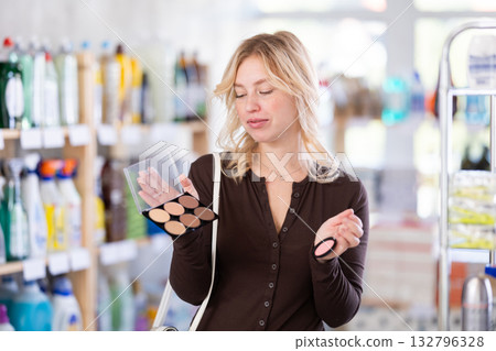 Beautiful young girl pondering and choosing face powder in cosmetics department in supermarket Beautiful young girl pondering and choosing face powder in cosmetics department in supermarket 132796328