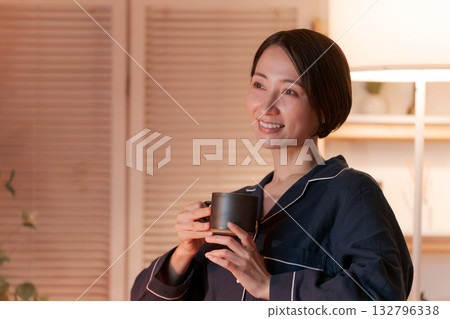 晚上，一位穿著睡衣的女子在房間裡喝著熱飲。 132796338