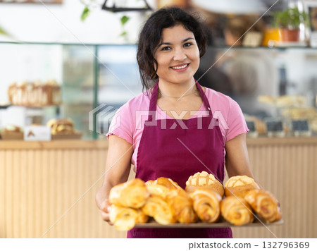 Positive female cafe employee carries tray with fresh croissants 132796369