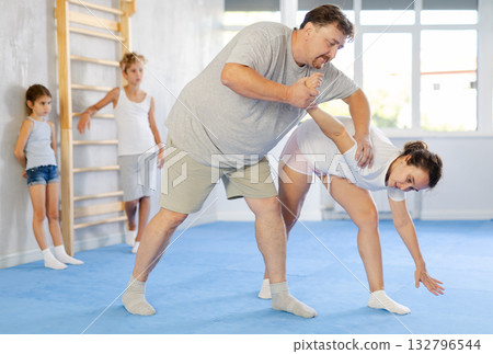 Self-defense lesson for the family - mom and dad practice doing painful power grip. Children are watching Self-defense lesson for the family - mom and dad practice doing painful power grip. Children are watching 132796544