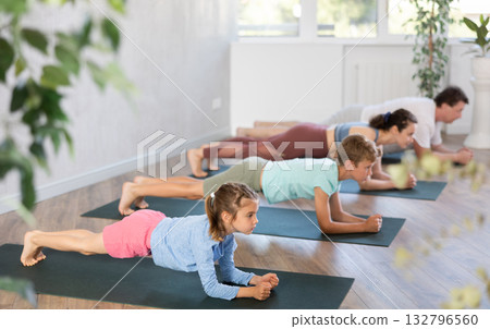 Pleasant little girl practicing plank pose of yoga with her family 132796560