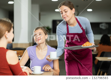 Polite waitress brings coffee and croissant to young girls in cafeteria Polite waitress brings coffee and croissant to young girls in cafeteria 132796565