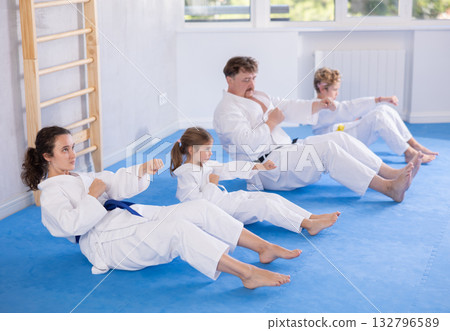 Family with preteen kids in kimonos performing core twist with punches Family with preteen kids in kimonos performing core twist with punches 132796589