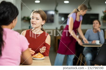 Young girl chatting with friend over coffee and croissant in cafeteria Young girl chatting with friend over coffee and croissant in cafeteria 132796590