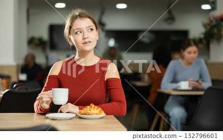 Young female sitting alone at table in cozy cafe, drinking fragrant coffee Young female sitting alone at table in cozy cafe, drinking fragrant coffee 132796601