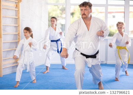 Children with parents in kimono standing in fight stance during group karate training in gym 132796621