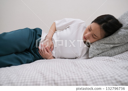 一名女子躺著,因胃痛摀著肚子。 一名女子躺著,因胃痛摀著肚子。 132796736