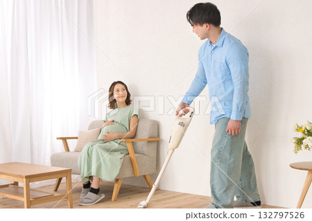 一位年輕男子一邊愉快地吸塵，一邊和孕婦聊天。 132797526