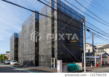 An apartment building covered in black netting due to exterior wall construction 132798159