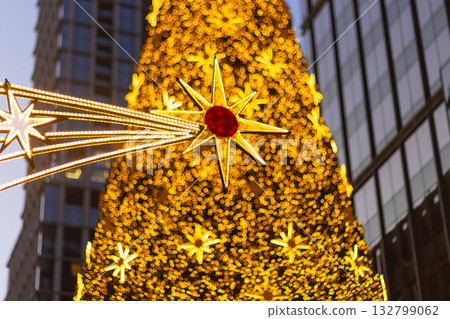 Christmas tree golden star decoration holiday. A close-up view of a festive outdoor tree covered in warm, yellow bokeh lights and a large, prominent, stylized star ornament 132799062