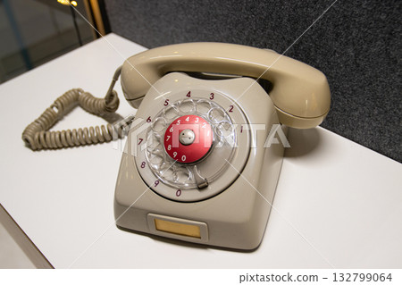 Vintage rotary telephone dial retro classic. A beige/grey antique telephone with a red center dial sits on a white surface, representing old technology and communication 132799064