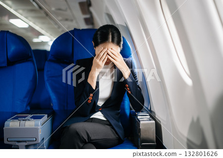 frustrated woman sitting on an airplane with her head in her hands. Asian woman sitting in a seat in airplane frustrated woman sitting on an airplane with her head in her hands. Asian woman sitting in a seat in airplane 132801626
