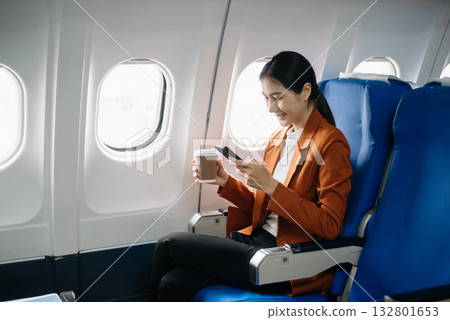 Asian businesswoman or entrepreneur in a formal suit on an airplane sitting in business class using a phone, computer laptop. Travel in style, work 132801653
