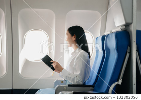 Attractive Asian female passenger of airplane sitting in comfortable seat while working laptop and tablet with mock up area using wireless connection. 132802056