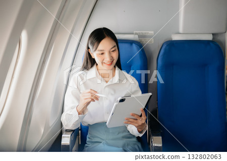 Young Asian executive excels in first class, multitasking with digital tablet, laptop and smartphone. Travel in style, work 132802063