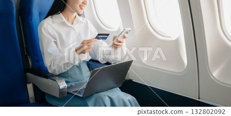 Young Asian executive excels in first class, multitasking with digital tablet, laptop and smartphone. Travel in style, work 132802092