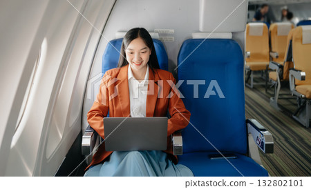 Attractive Asian female passenger of airplane sitting in comfortable seat while working laptop and tablet with mock up area using wireless connection. 132802101