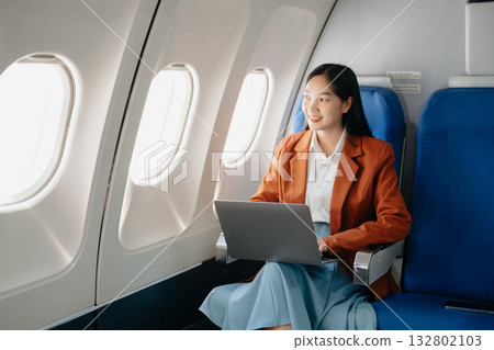 Attractive Asian female passenger of airplane sitting in comfortable seat while working laptop and tablet with mock up area using wireless connection. 132802103
