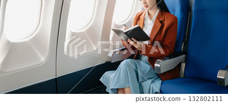 Attractive Asian female passenger of airplane sitting in comfortable seat while working laptop and tablet with mock up area using wireless connection. 132802111