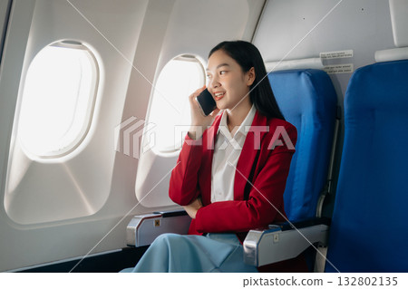Attractive Asian female passenger of airplane sitting in comfortable seat while working laptop and tablet with mock up area using wireless connection. 132802135