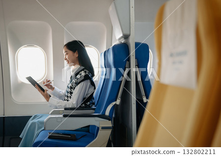 Attractive Asian female passenger of airplane sitting in comfortable seat while working laptop and tablet with mock up area using wireless connection. 132802211