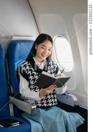 Attractive Asian female passenger of airplane sitting in comfortable seat while working laptop and tablet with mock up area using wireless connection. 132802215