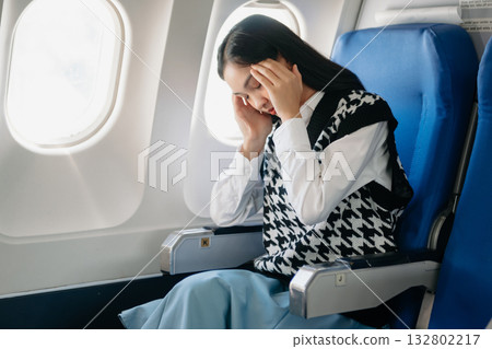 Photo of a frustrated woman sitting on an airplane with her head in her hands. woman sitting in a seat in airplane Photo of a frustrated woman sitting on an airplane with her head in her hands. woman sitting in a seat in airplane 132802217