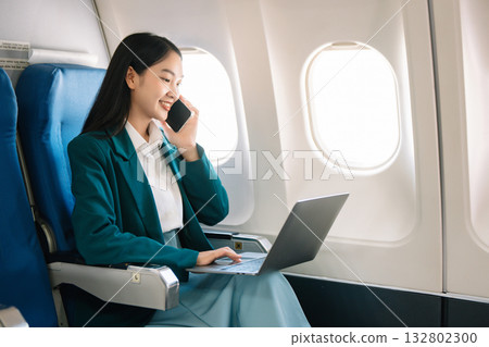 Attractive Asian female passenger of airplane sitting in comfortable seat while working laptop and tablet with mock up area using wireless connection. 132802300