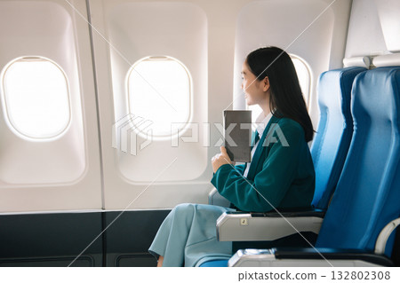 Attractive Asian female passenger of airplane sitting in comfortable seat while working laptop and tablet with mock up area using wireless connection. 132802308