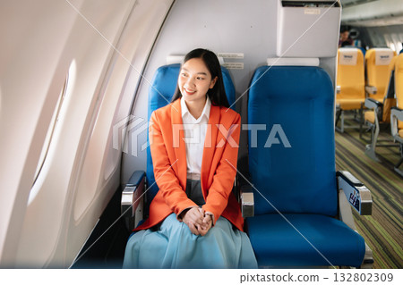 Attractive Asian female passenger of airplane sitting in comfortable seat while working laptop and tablet with mock up area using wireless connection. 132802309