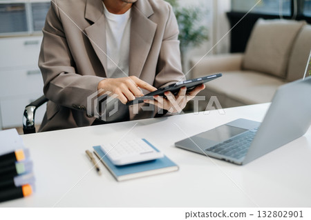 Young handsome man typing on tablet and laptop while sitting at the working table Young handsome man typing on tablet and laptop while sitting at the working table 132802901