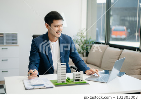 Young real estate agent worker working with laptop and tablet at table in office and small house 132803008