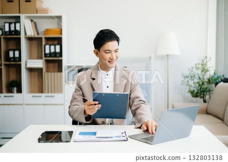 Young Asian man using laptop and tablet while sitting at her working place. Young Asian man using laptop and tablet while sitting at her working place. 132803138