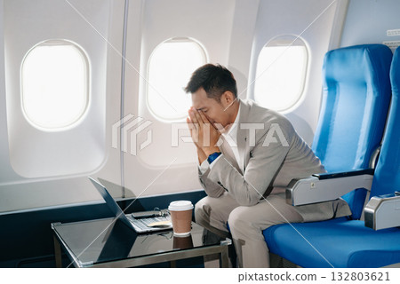 Photo of a frustrated man sitting on an airplane with her head in her hands. Asian Businessman sitting Photo of a frustrated man sitting on an airplane with her head in her hands. Asian Businessman sitting 132803621